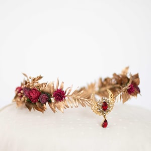 Peut inclure: Une couronne de feuilles d'or avec des fleurs bordeaux et un pendentif en pierre précieuse rouge.