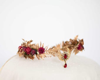 May include: A gold leaf crown with burgundy flowers and a dangling red gemstone pendant.