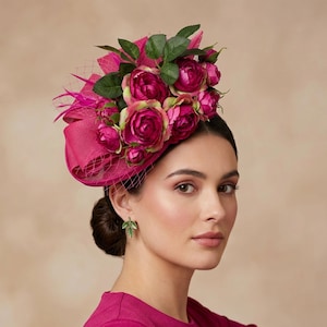 May include: A bright fuchsia hat decorated with pink roses and green foliage. The hat includes a mesh veil and feather detailing. This stylish headpiece is suitable for formal events and celebrations.