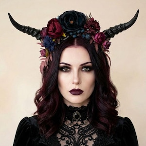 May include: A woman wearing a black horn headdress adorned with dark red and blue flowers. The horns are black and curved. She has dark red hair and is wearing a black lace choker and black dress.