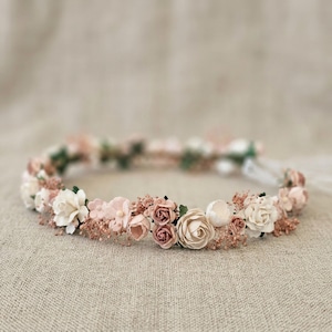May include: A floral crown featuring a variety of artificial flowers in shades of pink, cream, and mauve. The flowers are arranged in a circular pattern, creating a delicate and romantic headpiece. Perfect for weddings or special occasions.