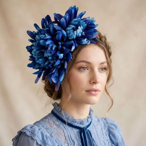 Puede incluir: Un gran accesorio para el cabello que presenta un grupo de vibrantes flores de crisantemo azules con pétalos en capas. Las flores de color azul intenso están dispuestas en una formación densa y redondeada, mostrando tonos de azul marino y real.