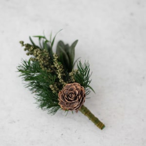 Könnte beinhalten: Ein kleiner Strauß aus Grünzeug und einer braunen Tannenzapfen, der zu einem Blumenmuster arrangiert ist.