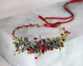 May include: A red and green Christmas wreath with red berries and frosted greenery. The wreath is tied with a red ribbon.