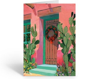May include: A greeting card featuring an illustration of a pink adobe-style building with a wooden door, a green door frame, and a Christmas wreath. Large green prickly pear cacti flank the entrance, with small colorful flowers at the base.