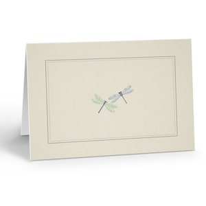 May include: A blank ivory card with a thin black border. Two blue and green dragonflies are centered on the card.
