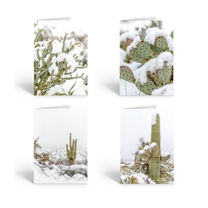 May include: Four greeting cards featuring different desert plants covered in snow. The cards are blank inside and ready for a personal message.