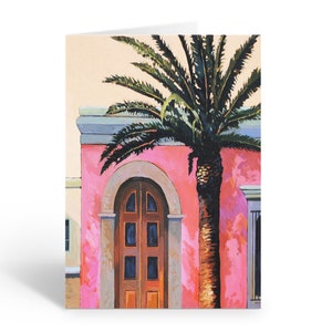 May include: A painting of a pink building with a brown door and a palm tree in front of it.
