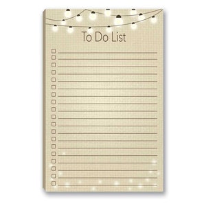 May include: A beige to-do list notepad with a string of lights at the top. The notepad has a lined surface and a white border. The text "To Do List" is printed in black at the top of the notepad.