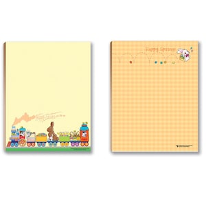 May include: Two yellow notepad sets with bunny illustrations. One notepad features a bunny train with the text "Happy Easter" and the other notepad features a bunny with a basket of eggs and the text "Happy Spring!"