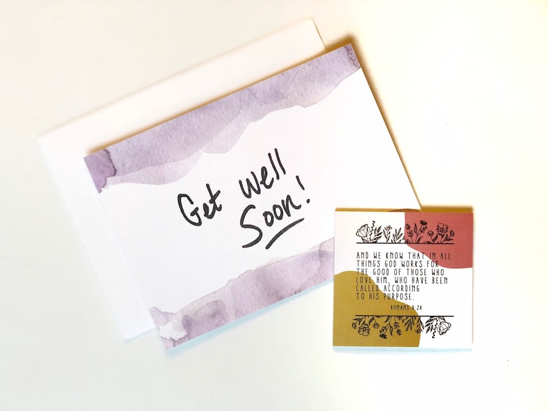 May include: A white greeting card with a watercolor design in shades of purple and the words "Get well Soon!" in black. A small square card with a floral design and text from Romans 8:28 is also present.