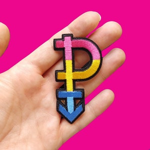 Könnte beinhalten: Ein gestickter Aufnäher mit einem Geschlechtsymbol mit einem nach unten zeigenden Pfeil in Pink, Gelb und Blau.