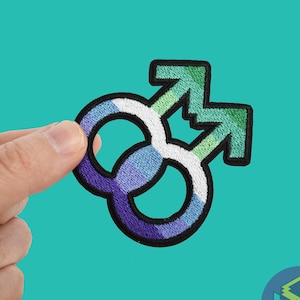 Puede incluir: Un parche bordado con dos símbolos masculinos entrelazados en verde, azul y morado.