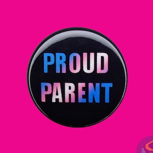 May include: A black button with the words "PROUD PARENT" in white letters with a blue, pink, and white gradient.