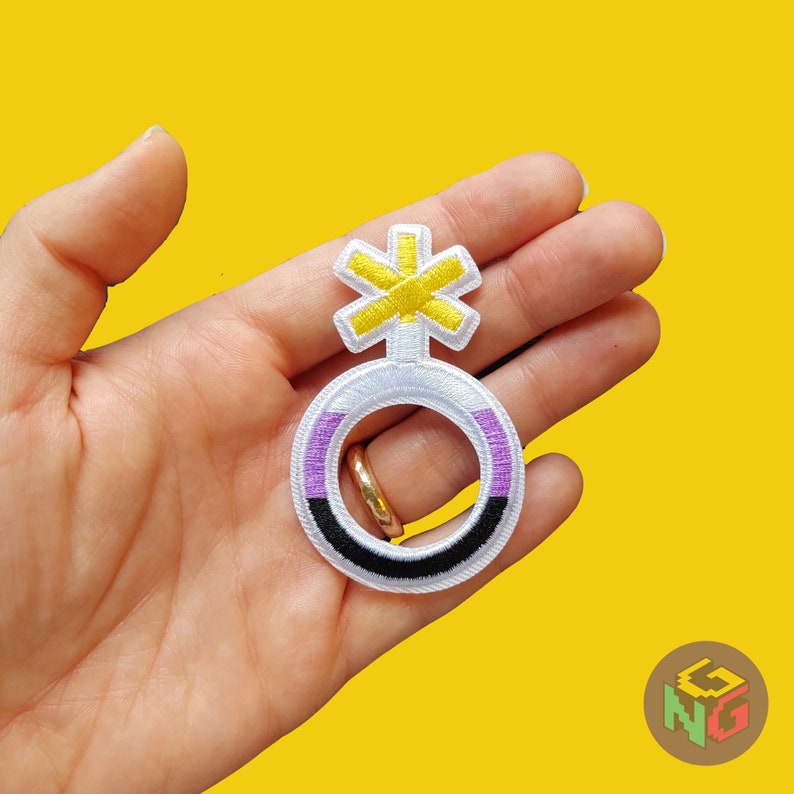 hand holding embroidered nonbinary symbol patch in front of yellow background