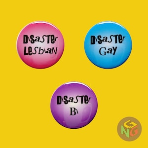 pink disaster lesbian pin, blue disaster gay button, purple disaster bi pin on yellow background