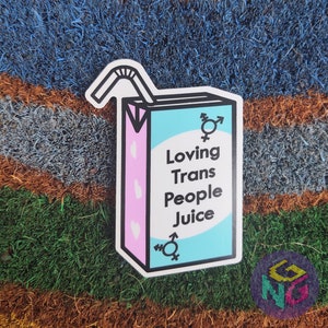 May include: A sticker of a cartoon juice box with a straw, pink and blue colors, and the text "Loving Trans People Juice".