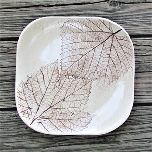 May include: A white ceramic rectangular dish with two brown leaf imprints. The leaves are detailed with veins and edges.