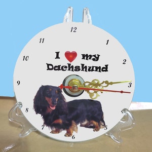 May include: White clock with black hands and a red heart. The clock face has the text "I love my Dachshund" and a black and tan Dachshund dog image.
