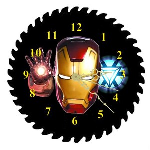 May include: A round wall clock featuring an Iron Man theme. The clock face is a black saw blade with yellow numerals. The center features Iron Man's helmet and hand, with a blue and white energy symbol. The clock hands are gold.