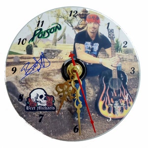 May include: A clock with a picture of Bret Michaels from the band Poison. The clock face is a CD with a picture of Bret Michaels sitting on a rock with a guitar. The clock face also has the band's name "Poison" and Bret Michaels' signature. The clock hands are gold and red.