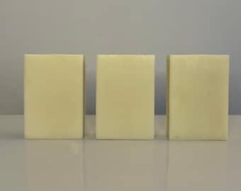 May include: Three rectangular bars of white soap, arranged in a row on a white surface.