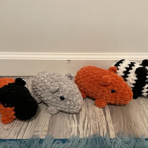 May include: Four crocheted stuffed animals in the shape of guinea pigs. The guinea pigs are in various colors, including black, white, orange, and gray.