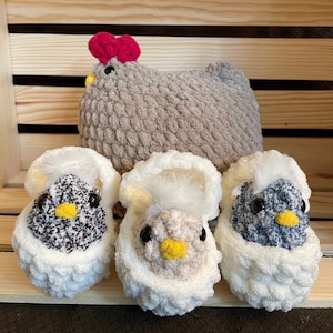 May include: Three crocheted chick toys. One is a larger grey hen with a pink comb. The other two are smaller chicks in white nests with black, beige, and blue details.
