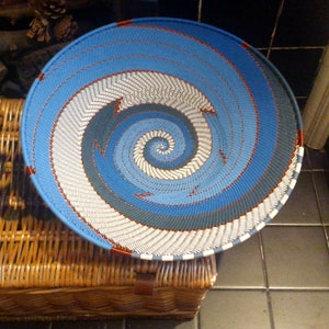 May include: A blue and white woven basket with a spiral pattern. The basket is made of natural materials and has a red rim.