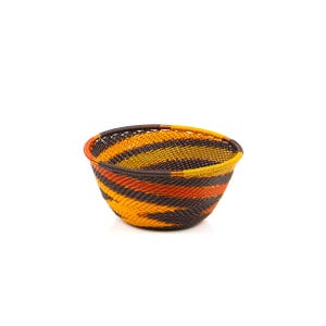 May include: A woven basket with a rounded shape, featuring a vibrant color scheme. The basket's design incorporates bands of orange, yellow, and brown, creating a visually appealing pattern. The rim is reinforced with a darker brown material.