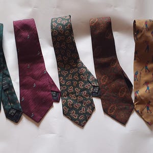 May include: Five neckties in various patterns and colors. The ties include a dark green tie with small white dots, a burgundy tie with a subtle pattern, a green paisley tie, a brown tie with a floral design, and a tan tie with golf figures.