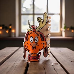 May include: A wooden height chart featuring a cartoon dog character with antlers. The dog is orange with black and red accents. The height chart is made of light brown wood and has a notched edge for marking height measurements.