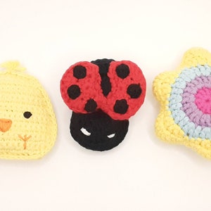May include: Three crocheted stuffed toys: a yellow chick, a red and black ladybug, and a yellow flower with a pink, purple, and blue center.