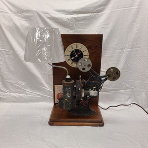 May include: A vintage film projector lamp with a white lampshade, a clock face, and a wooden base.