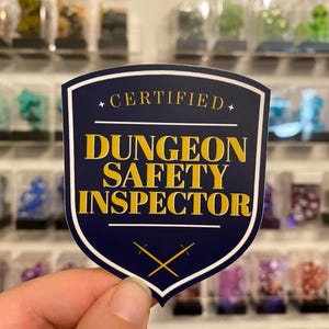 May include: A blue and white shield-shaped sticker with gold text that reads "Certified Dungeon Safety Inspector".