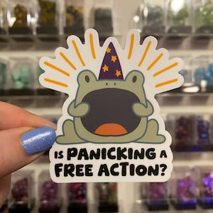 May include: A sticker depicting a cartoon frog with a wide open mouth, wearing a purple wizard's hat with gold stars. The frog is surrounded by orange rays, with the text "Is Panicking a Free Action?" in black.