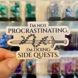 May include: White sticker with black text and a sword design. The text reads "I'm not procrastinating, I'm doing side quests."