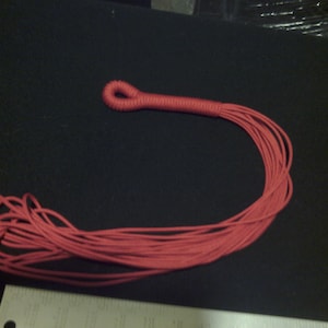 Pode incluir: Um chicote de corda trançada vermelha com um laço na ponta.