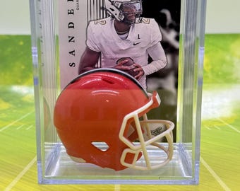 May include: A clear plastic display case with a red and white miniature football helmet inside. The case also contains a trading card featuring a football player wearing a white jersey with the number 9 and the name "SAN DERRS" printed on the card. The card also has the word "ROOKIE" printed on it.