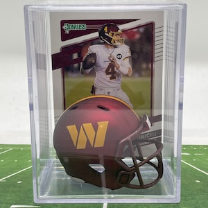 May include: A clear plastic display case containing a burgundy and gold football helmet. The helmet has a white "W" on the side. The case also includes a football card featuring a player in a burgundy and gold uniform. The card displays the text "Donruss 21".