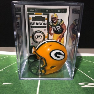 May include: A Green Bay Packers football helmet miniature in a clear plastic display case with a Green Bay Packers trading card featuring a player wearing the number 92. The card has the text "SEASON" and "GREEN BAY PACKERS".