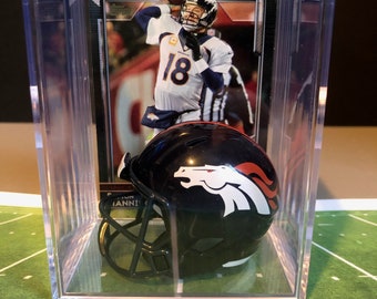 May include: A black and orange Denver Broncos mini football helmet in a clear plastic display case. The helmet has a white horse logo on the side. The case also includes a trading card of a Denver Broncos player.