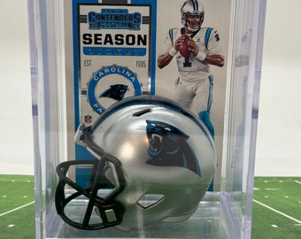 Könnte beinhalten: Ein silberner Carolina Panthers Mini-Helm in einer durchsichtigen Plastikvitrine mit einer Panini Contenders Season Ticket Karte, die einen Carolina Panthers Spieler zeigt. Die Karte trägt den Text "SECTION 245 | ROW 65 | SEAT 1" und "EST. 1995".