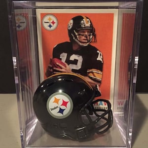 May include: A black and yellow miniature football helmet with the Pittsburgh Steelers logo. The helmet is in a clear plastic display case with a vintage football card of a Steelers player.