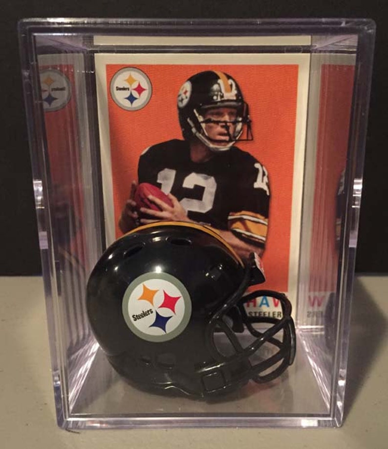 May include: A black and yellow miniature football helmet with the Pittsburgh Steelers logo. The helmet is in a clear plastic display case with a vintage football card of a Steelers player.