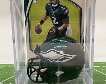 May include: A green and black miniature football helmet with a white wing logo. The helmet is in a clear plastic display case with a football card featuring a player in a green and white uniform. The card has the text "Absolute Football" on it.