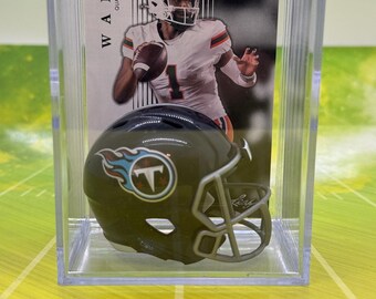 May include: A clear plastic display case with a miniature football helmet inside. The helmet is dark green with a blue and white Tennessee Titans logo. The case also contains a trading card with a photo of a football player wearing a white jersey with the number 1. The card reads "WARD QUARTERBACK ROOKIE".