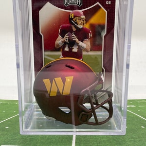 May include: A clear plastic display case with a burgundy and gold football helmet inside. The helmet has a white "W" on the side. The case also contains a burgundy and gold football card with a player wearing a burgundy and gold uniform. The card has the text "PLAYOFF" and "QB" on it.