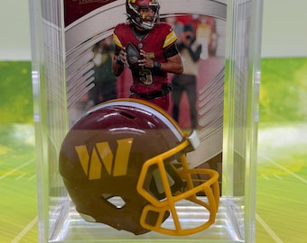 May include: A miniature burgundy and gold football helmet with a yellow facemask and a large yellow W logo, displayed in a clear plastic case in front of an Absolute Football trading card featuring a player in a burgundy uniform holding a ball.