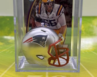 May include: A silver and red miniature football helmet in a clear plastic display case with a football card featuring a player in a purple and gold uniform. The card has the text "Bowman Chrome" and "1st Bowman".